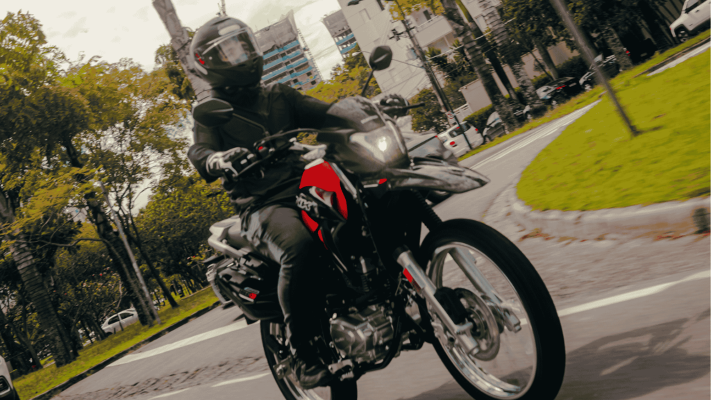 Motociclista com capacete pilotando a nova Haojue NK 160 preta e vermelha com faróis acesos na cidade.