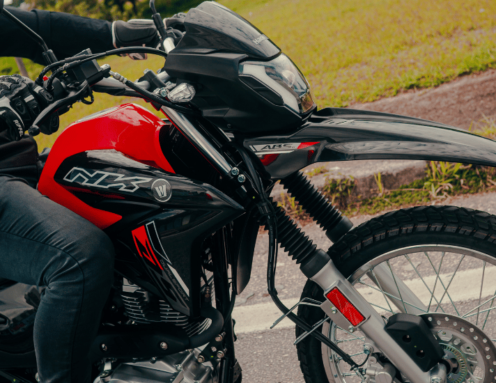 Motociclista pilotando a nova Haojue NK 160 preta e vermelha com faróis acesos na cidade.